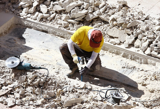 Obrero con martillo mazo y cincel picando suelo en reforma con radial y cable entre piedras, cascotes y escombros