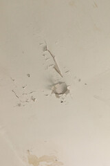 Ceiling of an old house displays noticeable cracks and peeling paint, indicating long-term neglect and deterioration. The surrounding environment feels neglected and abandoned