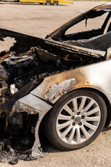 A car with extensive fire damage is parked in a lot. The charred interior reveals the aftermath of...