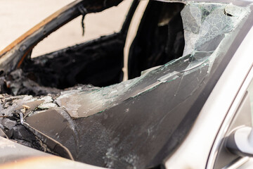 A burnt car is visible with shattered glass and damage to the interior. Signs of fire are evident...