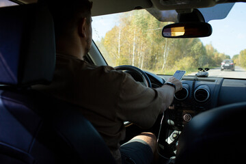 A man in a car checks the road using a navigator from a mobile phone