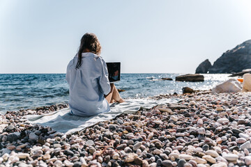 Remote work, digital nomad, pebble beach. Woman working on laptop on a sunny coast, enjoying...
