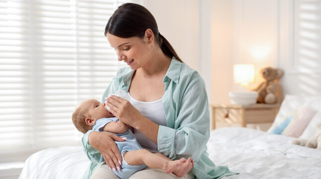 Fototapeta Mother feeding her newborn baby with bottle on bed at home