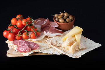Antipasti italiani con olive, formaggio e prosciutto e pane carasau  su sfondo nero