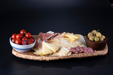 pane carasau con salame, formaggio e olive su vassoio in sughero sfondo nero