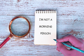A hand holds a pen above a notepad displaying the phrase I am not a morning person. A magnifying...
