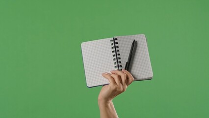 A woman hand holding an open notebook and pen on a green chroma key background. Shot for designs related to office, business, education and training.