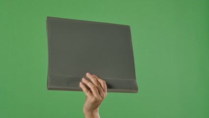 A woman hand holding a gray office folder with documents on a green chroma key background. Shot for designs related to office, business, education, and training.