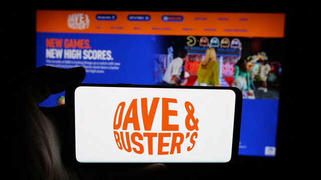 Stuttgart, Germany - 10-13-2025: Person holding cellphone with logo of company Dave and Buster's Entertainment Inc. on screen in front of webpage. Focus on phone display.
