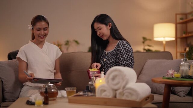 Asian adult women exchanging spa gift card at home relaxed cozy evening wellness friendship beautiful ladies enjoying personal self care