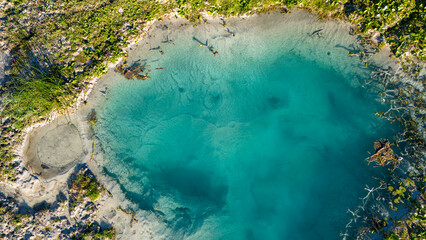 A beautiful drone shot looking down at a pristine natural pool where turquoise water fills a geologically rich basin creating a breathtaking and serene scene of untouched nature