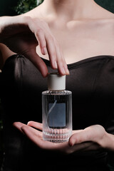 Graceful hands holding a luxurious perfume bottle. In the photo, beautiful female hands are holding an elegant glass bottle without a logo
