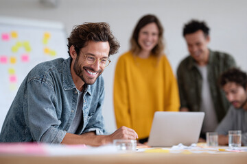 Smiling man leading a team in a modern office space, using a laptop. Illustrates collaboration, innovation, success, and positive work environment. For business, technology, or teamwork.