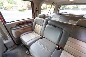 Rear two row beige leather bench seats, interior of an older 2004 American 4x4 family suv truck.   Shown in natural daylight, highlighting clean and well-preserved cabin details, speakers, armrests 