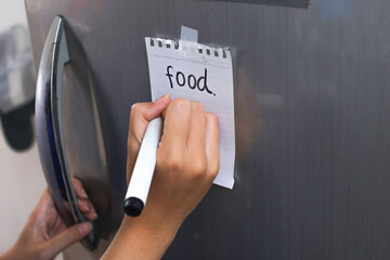 Writes Food On Notepad Stuck To Modern Refrigerator Door