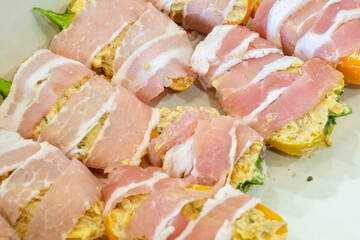 Raw bacon wrapped around stuffed jalapeño and mini pepper halves, ready to be cooked as homemade jalapeño poppers appetizer.