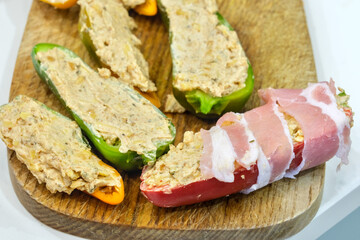 Raw bacon wrapped around stuffed jalapeño and mini pepper halves, ready to be cooked as homemade jalapeño poppers appetizer.