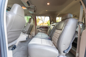 Rear two row beige leather bench seats, interior of an older 2004 American 4x4 family suv truck.   Shown in natural daylight, highlighting clean and well-preserved cabin details, speakers, armrests 