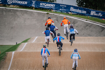 Fototapeta premium Valmiera, Latvia - July 12, 2025: BMX racers competing on track with vibrant colors and dynamic motion in the background. BMX European championships