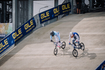 Fototapeta premium Valmiera, Latvia - July 12, 2025: Two male BMX riders racing on dirt track with ALE branding in background. BMX European championships
