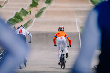 Fototapeta premium Valmiera, Latvia - July 12, 2025: BMX racers competing on track with vibrant colors and dynamic motion in background. BMX European championships