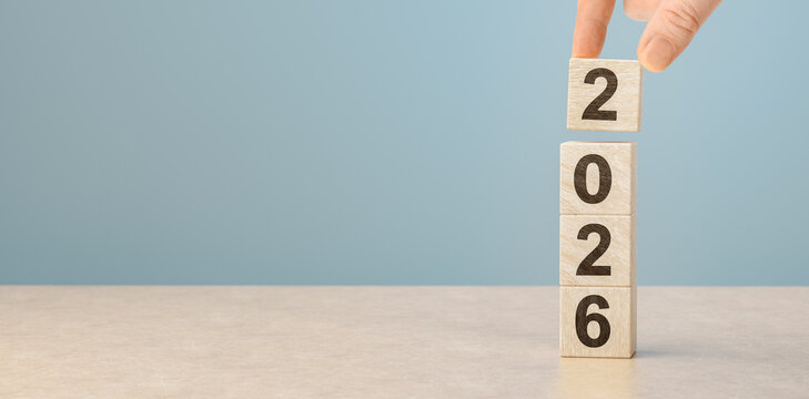 Hand building 2026 new year concept with wooden blocks. Male hand placing number two on stack of wood cubes