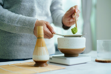 Woman sifting matcha powder into bowl on digital scale.