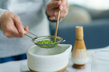 Woman sifting matcha powder into bowl on digital scale.