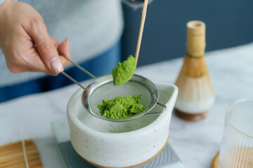 Woman sifting matcha powder into bowl on digital scale.