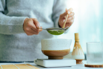Woman sifting matcha powder into bowl on digital scale.