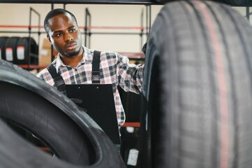 Portrait of African american warehouse worker standing by the pile of new car tires