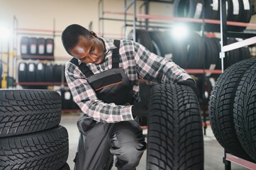 Car tire service concept. Portrait African american man mechanic holding new tyre on background...