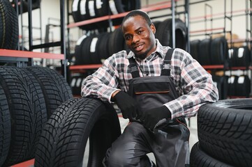 Portrait of African american warehouse worker standing by the pile of new car tires