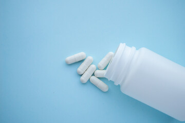 medicine pills capsule spilling out of bottle on blue background