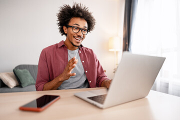 Smiling, positive African American man, freelancer having video call using laptop working at home