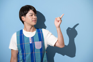エプロンを着て指差しのポイントポーズをする男性　保育士・介護士などのイメージ　水色背景