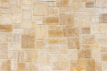 Background or texture of a wall with horizontal masonry of rectangular blocks of sandstone or limestone in beige and golden colors with a thin line of cement mortar, natural building material