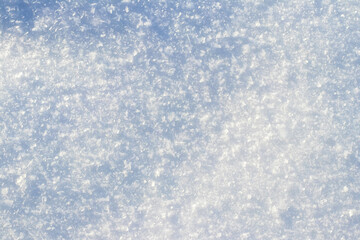 Detailed abstract background of fresh snow cover with icy crystals sparkling in the winter sun, with a blue tint and soft shadows, perfect for winter design and advertising
