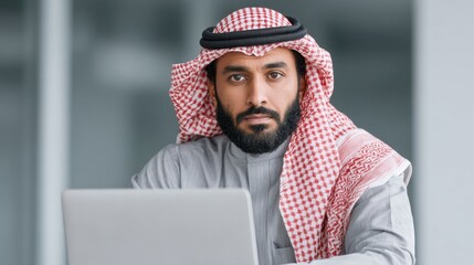 Young Middle Eastern Man Wearing Traditional Attire Working on Laptop in Modern Office Environment