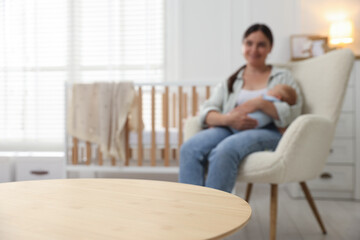 Fototapeta premium Happy mother and her baby on armchair at home, focus on wooden table, space for text