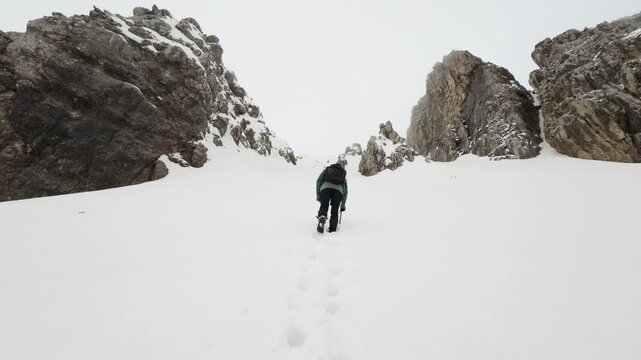 Mountaineer climbing a snowy couloir between steep rocky walls in winter conditions.
