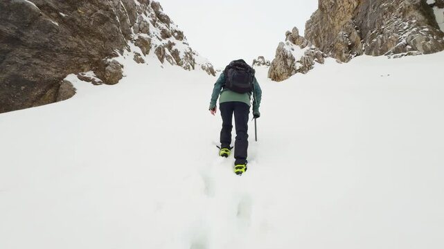 Mountaineer climbing a snowy couloir between steep rocky walls in winter conditions.