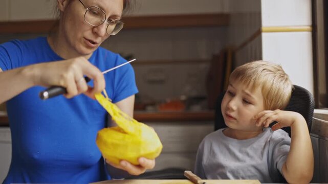 Mother peeling a mango fruit with a knife for her son