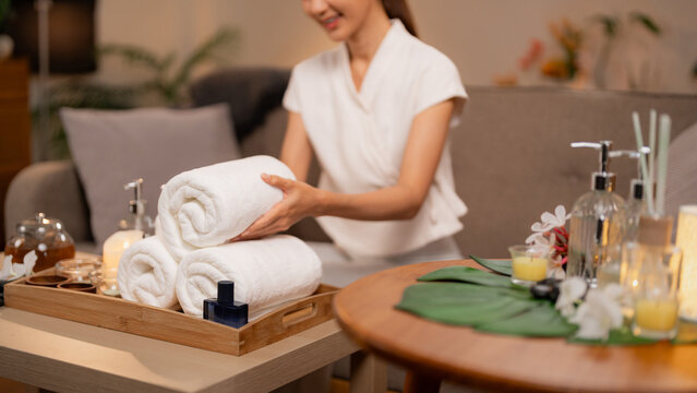 Adult Asian woman hands gently arrange rolled towels for spa treatment relaxing home wellness session promoting calm self care routine