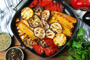 Tasty grilled vegetables in pan, spices and parsley on wooden table, flat lay