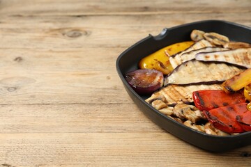 Tasty grilled vegetables and mushrooms in pan on wooden table, closeup. Space for text