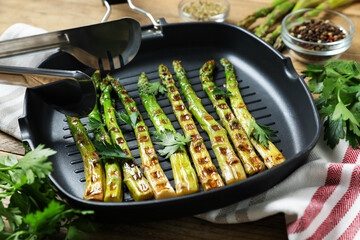 Delicious grilled asparagus in pan, spices and tongs on table, closeup