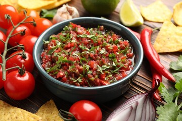 Tasty salsa sauce with nachos and ingredients on wooden table, closeup