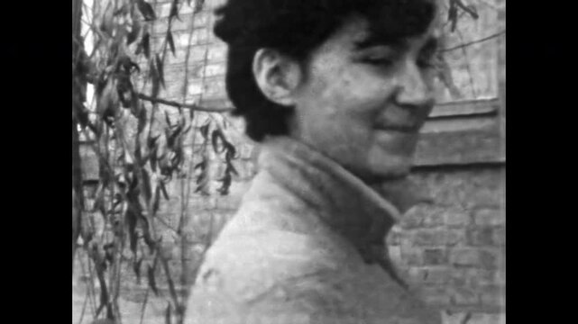 Happy young woman steps out of house, smiling bright, portrait of joyful face, cheerful posture and relaxed presence, natural beauty in vintage frame. Old film. Archival retro 1960s. Vintage archive.