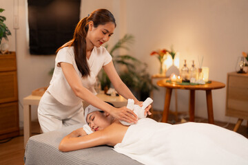 Asian adult women therapist provides hot herbal compress massage to client promoting relaxation...